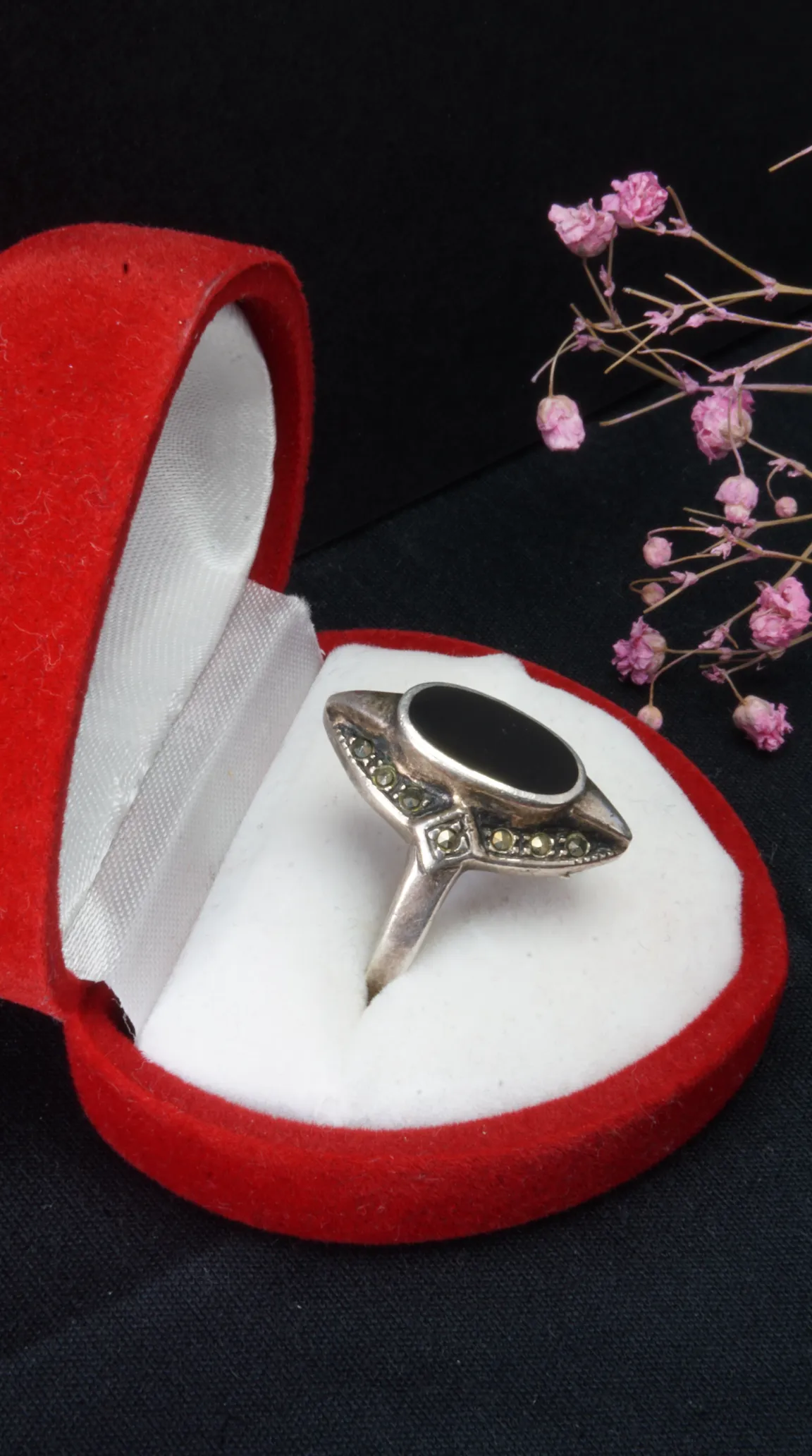 Vintage sterling silver ring with oval black onyx and marcasite details, displayed in a red heart-shaped jewelry box.