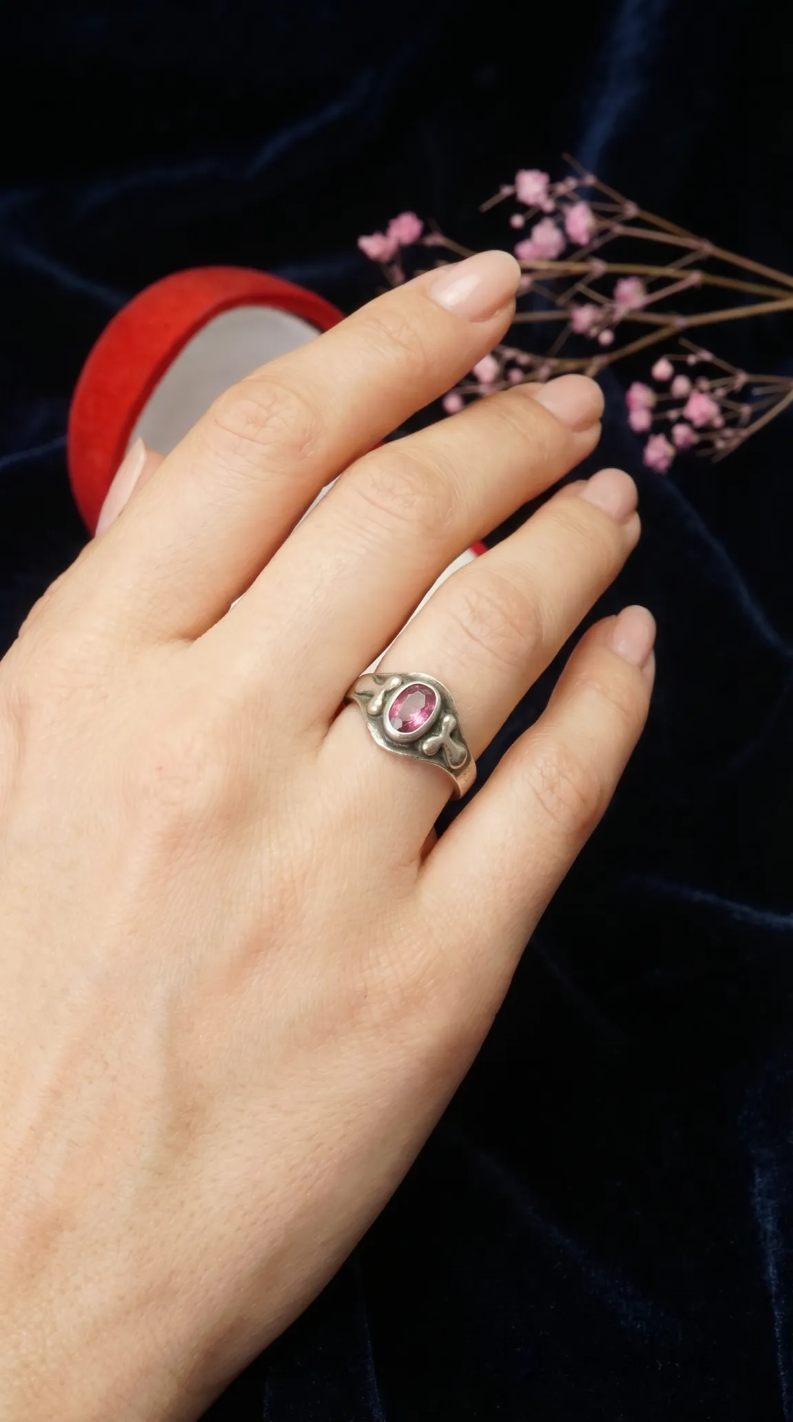 Vintage silver ring with oval pink gemstone, ornate antique style, worn on a hand.