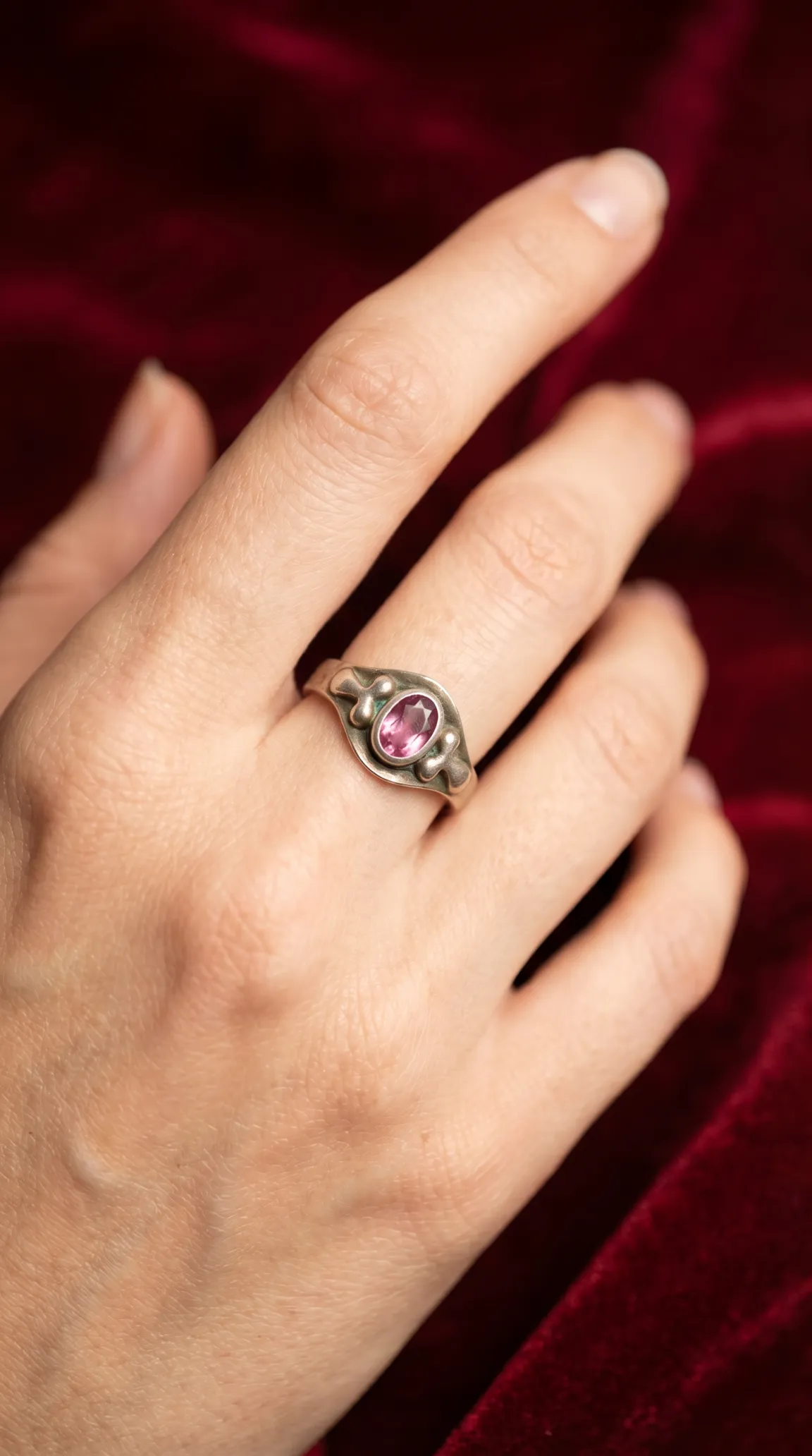 Vintage sterling silver ring with oval pink gemstone in Art Nouveau style setting, worn on a hand against red velvet background.