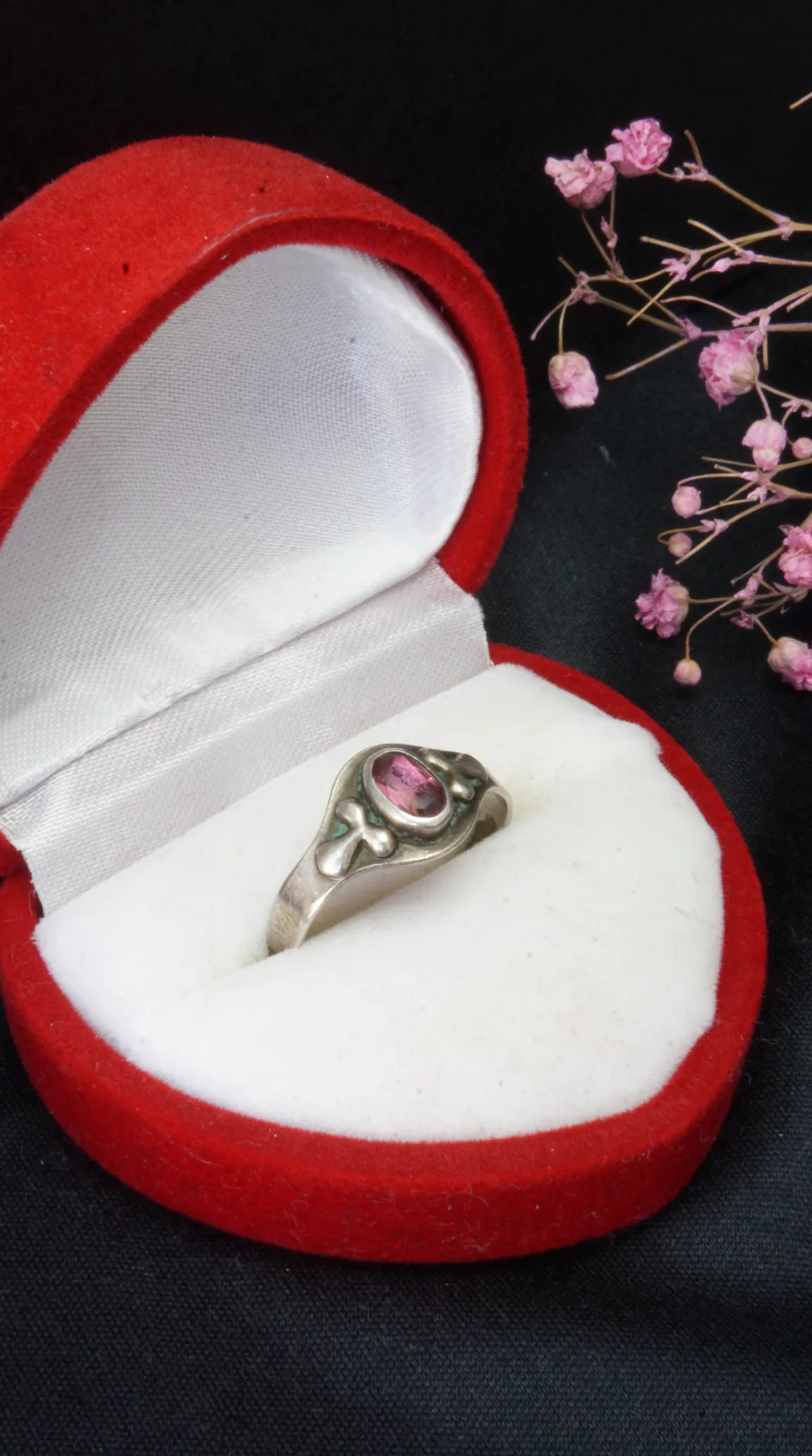 Vintage sterling silver ring with oval pink gemstone and decorative band in a red velvet heart-shaped box.