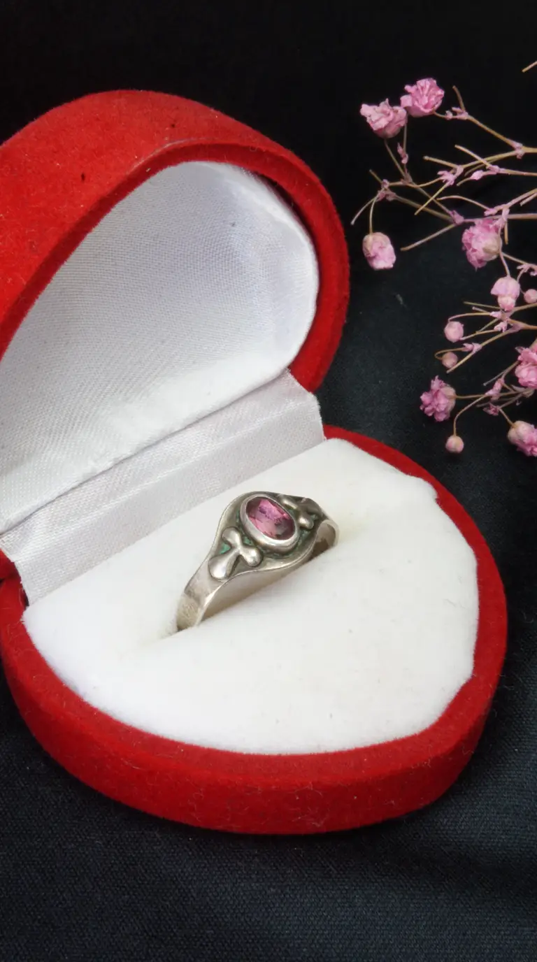 Vintage sterling silver ring with oval pink gemstone and decorative band in a red velvet heart-shaped box.