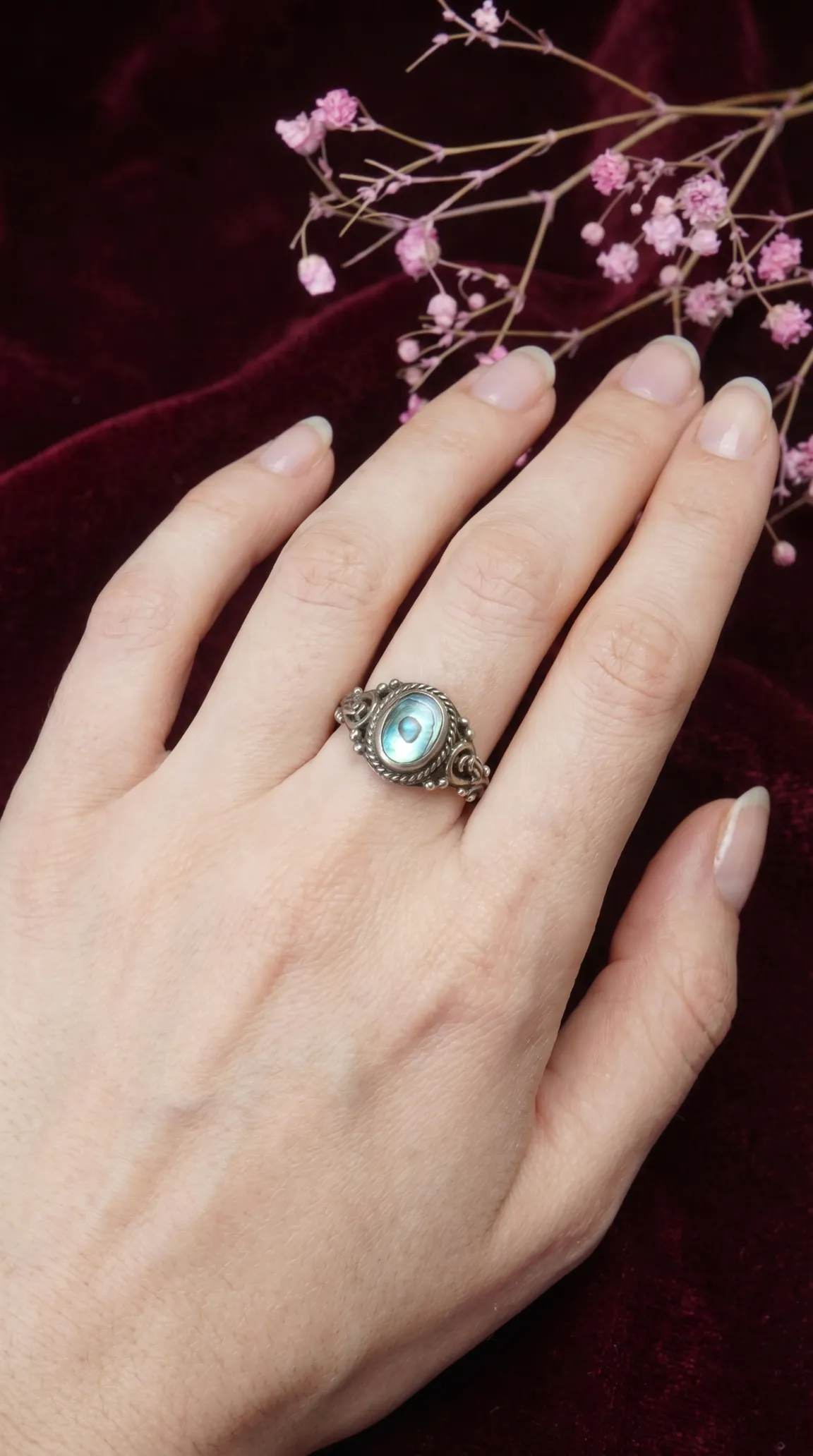 Vintage sterling silver abalone ring with intricate details, featuring an iridescent oval shell gemstone, worn on a hand.