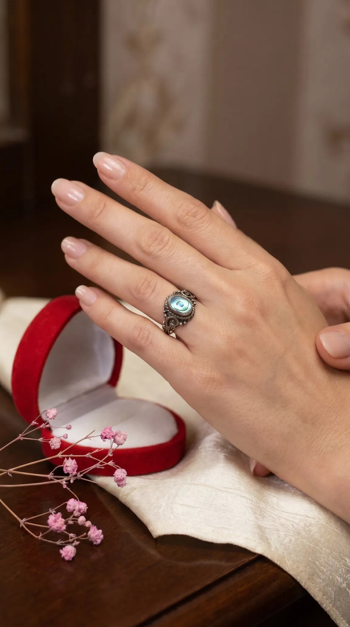 Vintage ornate abalone ring on woman's hand, next to open red velvet gift box.