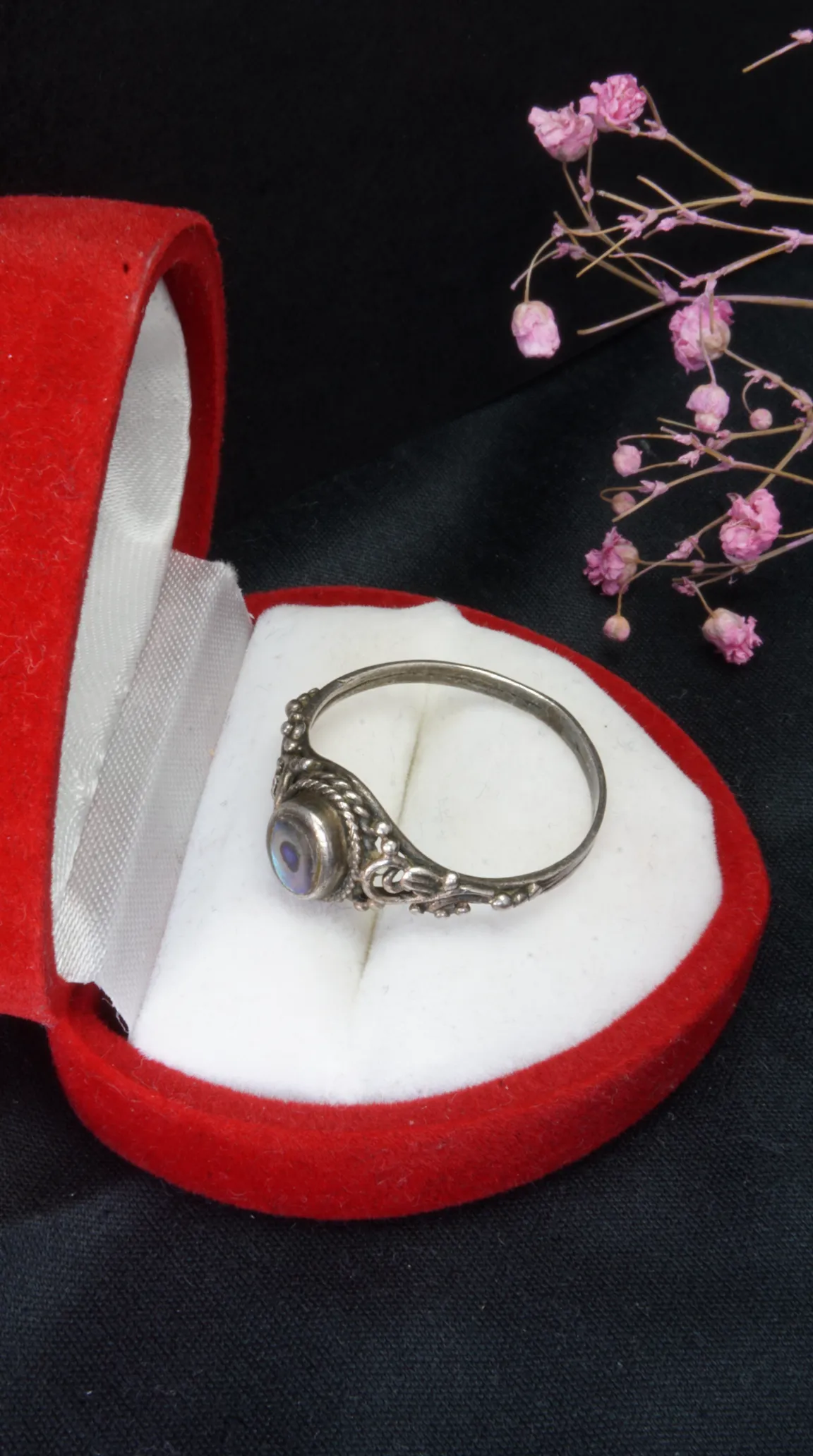 Vintage ornate silver ring with iridescent oval gemstone inside a red velvet ring box.