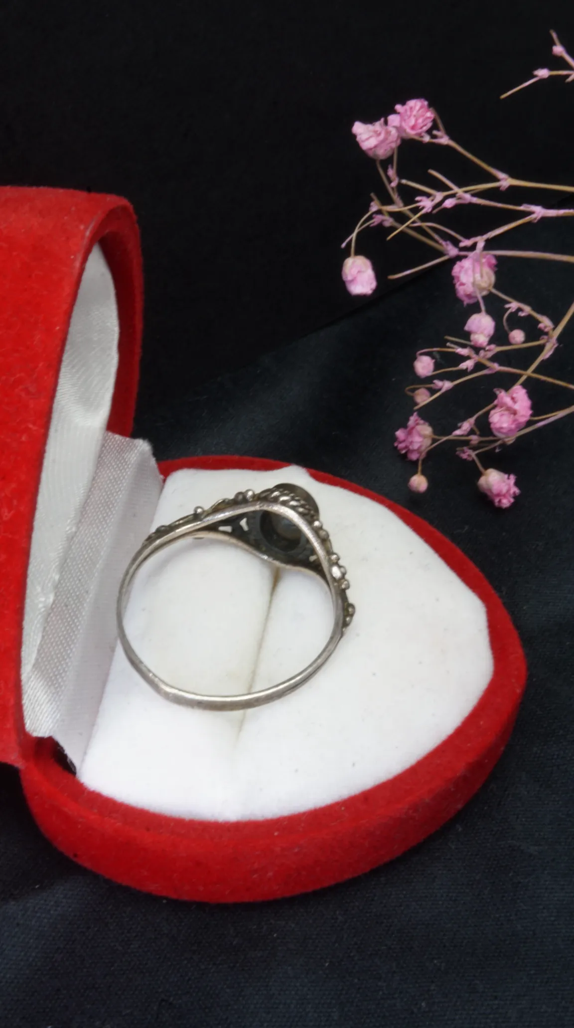 Vintage ornate silver ring with dark oval gemstone in a red heart-shaped jewelry box.