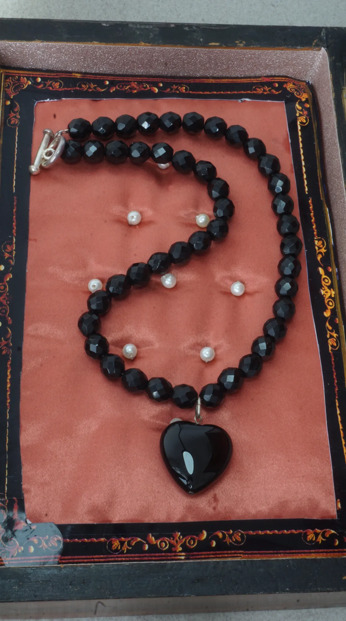 Vintage black faceted onyx bead necklace with polished black heart pendant and silver toggle clasp, displayed in an ornate presentation box.