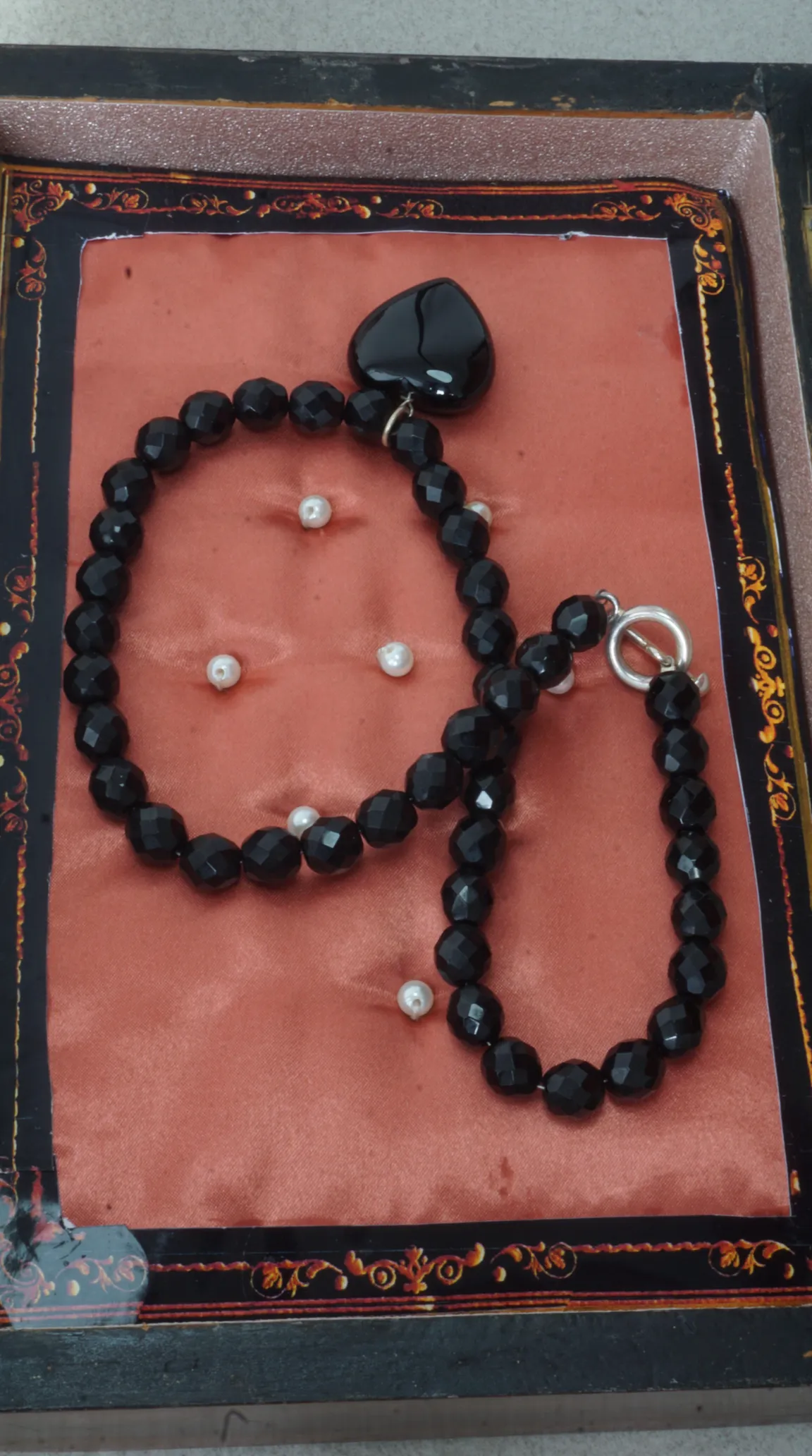 Vintage black faceted bead necklace and matching bracelet set with heart pendant and silver toggle clasp, displayed on coral fabric with pearl accents in an ornate box.