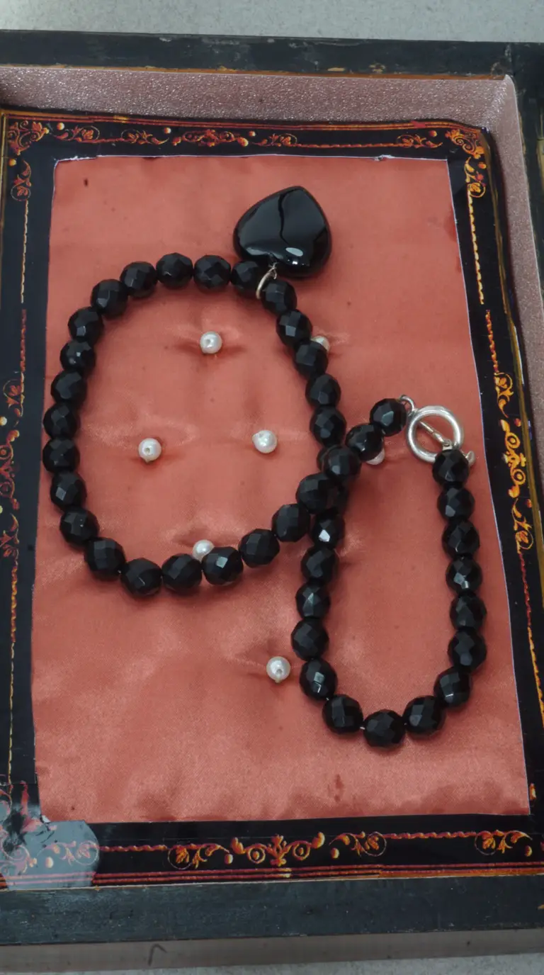 Vintage black faceted bead necklace and matching bracelet set with heart pendant and silver toggle clasp, displayed on coral fabric with pearl accents in an ornate box.