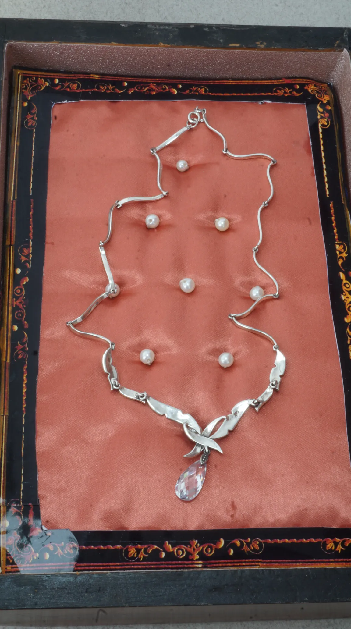 Vintage silver wavy link necklace with faceted crystal teardrop pendant, displayed in an ornate box with loose pearls.