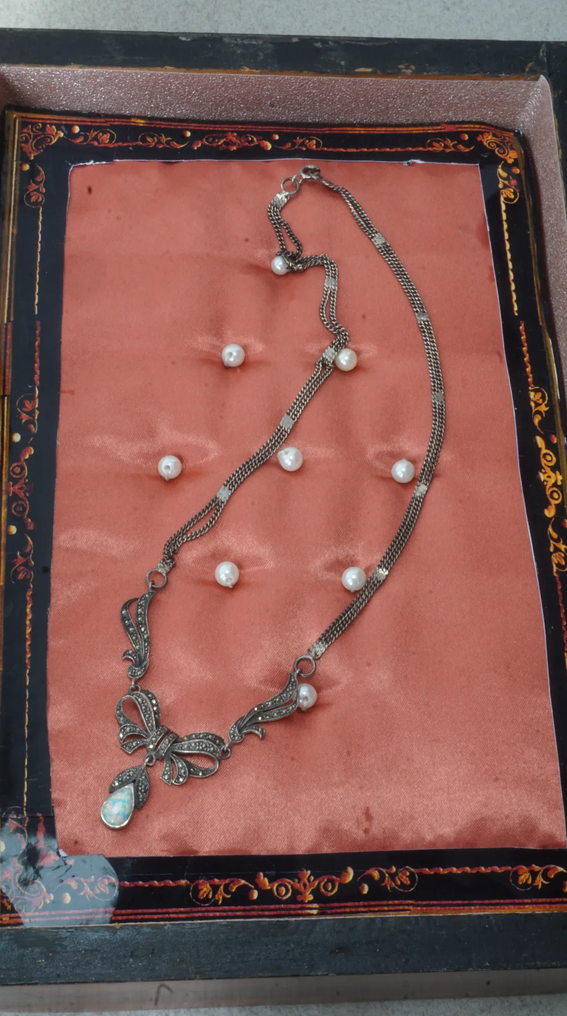 Vintage silver marcasite bow necklace with opal teardrop pendant and pearl accents on a pink satin background.