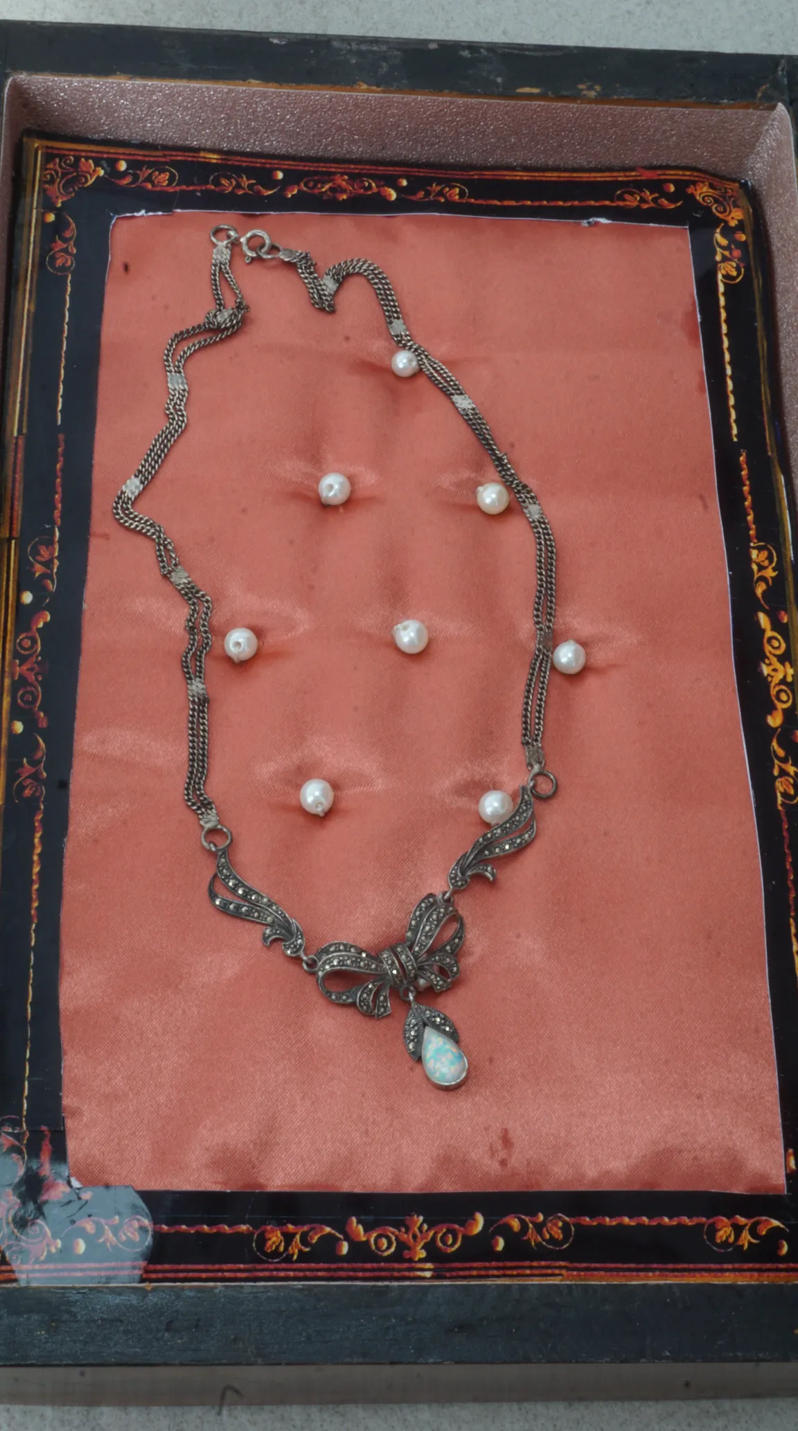Vintage sterling silver marcasite bow necklace with teardrop opal pendant, displayed on pink satin.