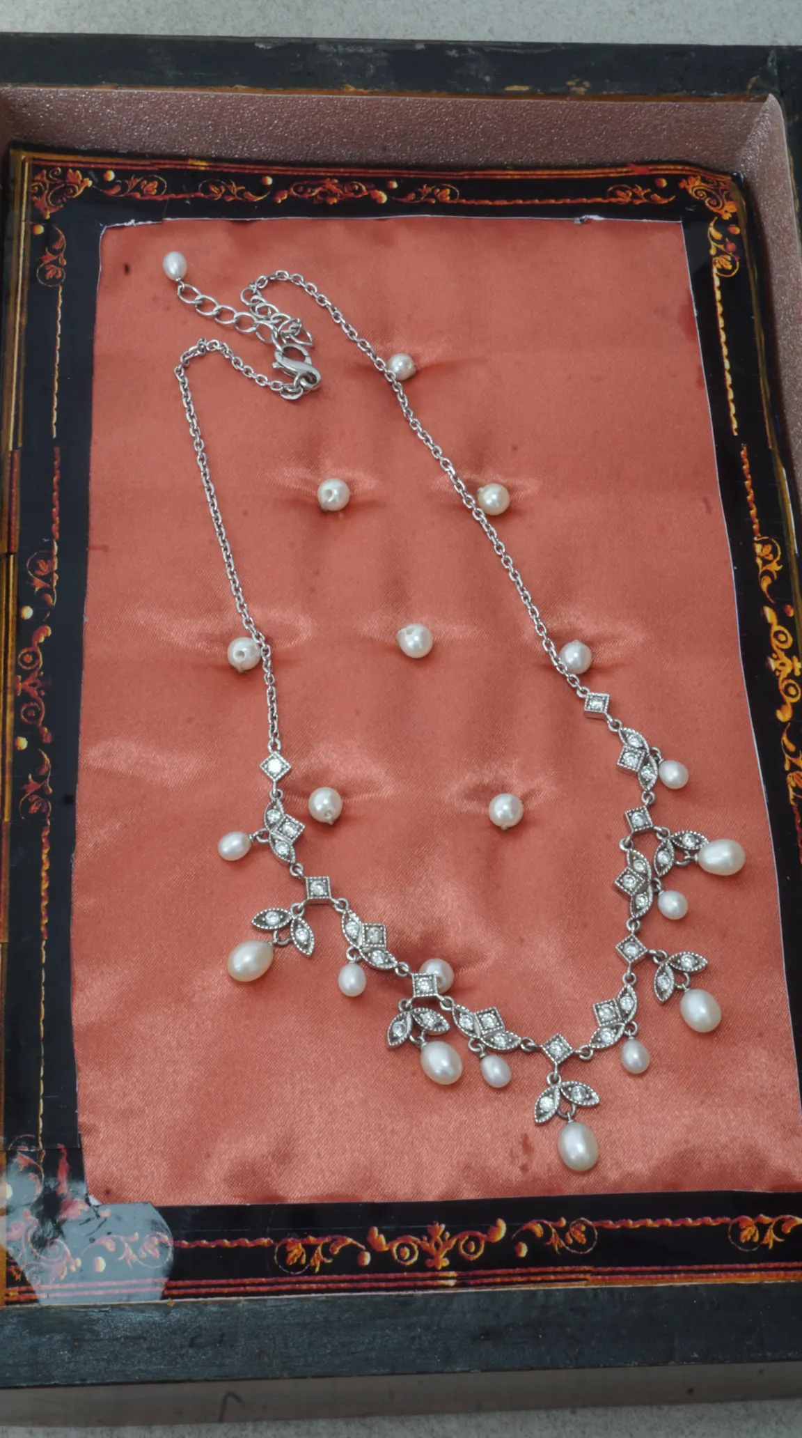 Vintage silver necklace with pearl drops, crystal accents, and ornate design, displayed on peach satin.