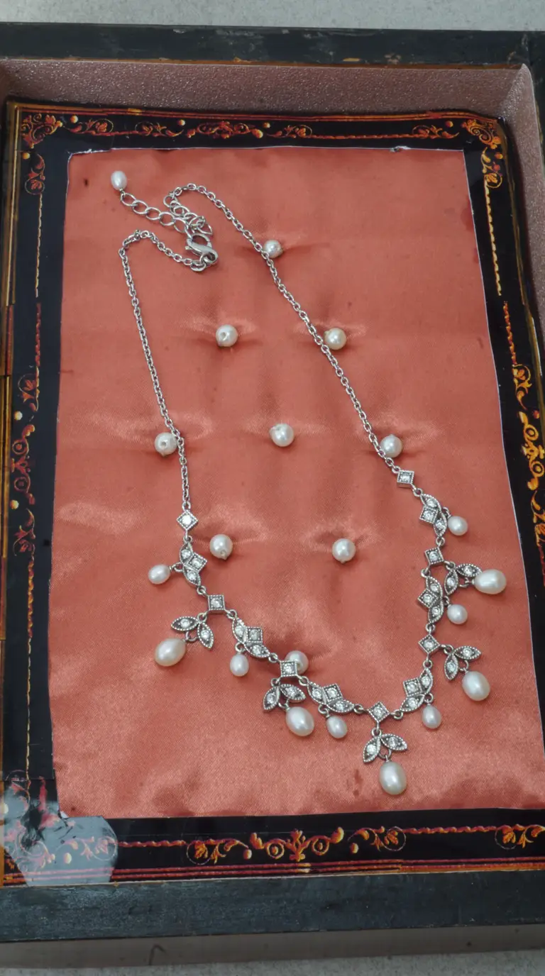 Vintage silver necklace with pearl drops, crystal accents, and ornate design, displayed on peach satin.