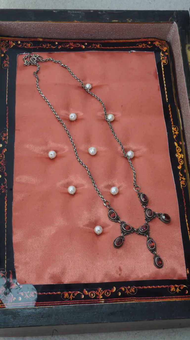 Vintage oxidized silver necklace with ornate red garnet gemstone pendant, displayed on peach satin.