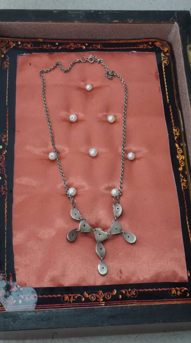 Vintage silver tone necklace with small pearls and abstract metal drop charms, displayed in an antique jewelry box with pink satin lining.