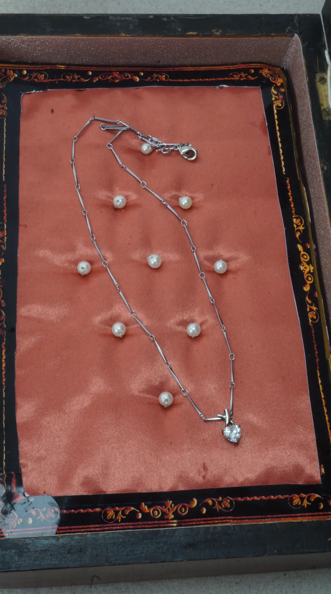 Vintage silver chain necklace with sparkling heart gemstone pendant, displayed with loose pearls on a salmon satin cushion in an antique decorated box.