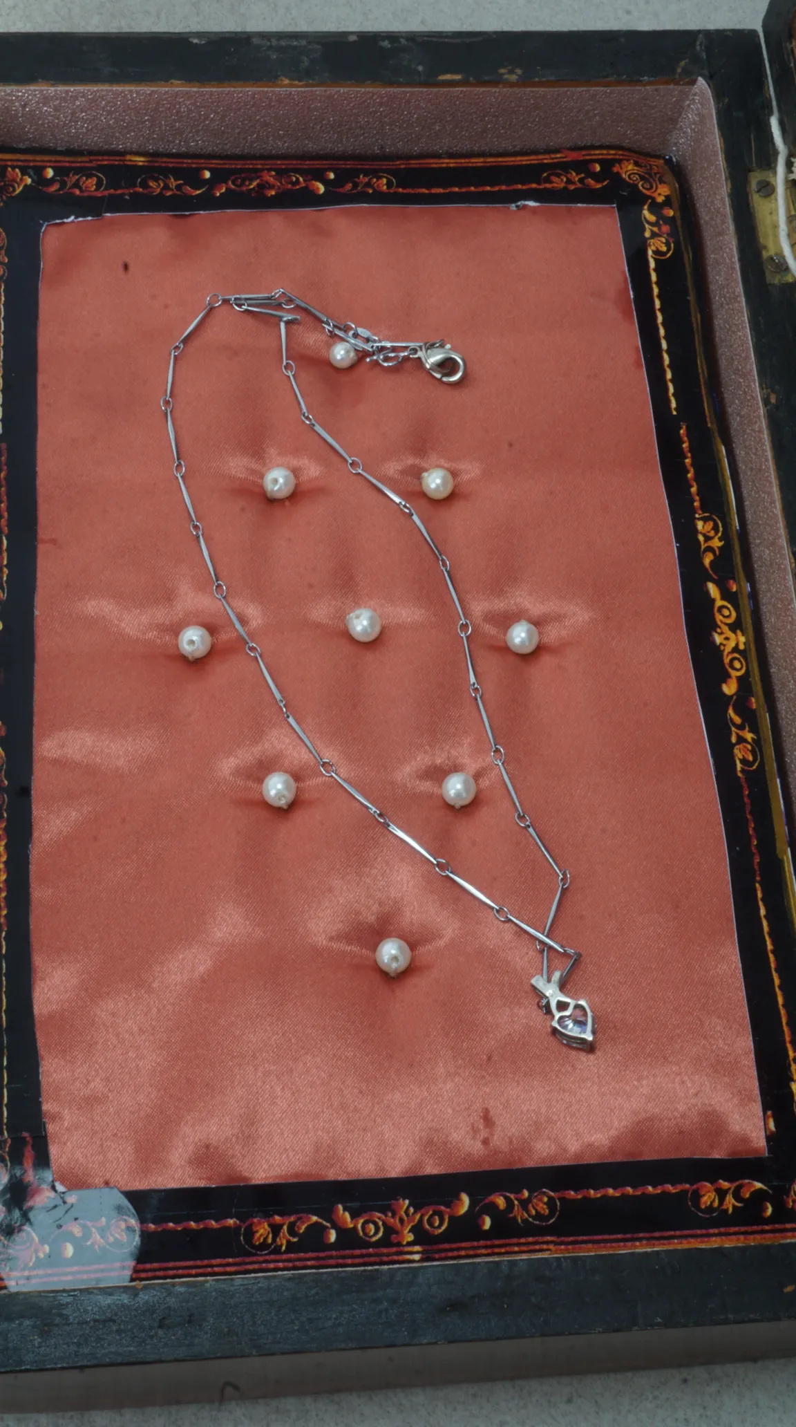 Vintage silver bar-link necklace with purple gemstone pendant, displayed on peach satin in an ornate antique jewelry box with scattered pearls.