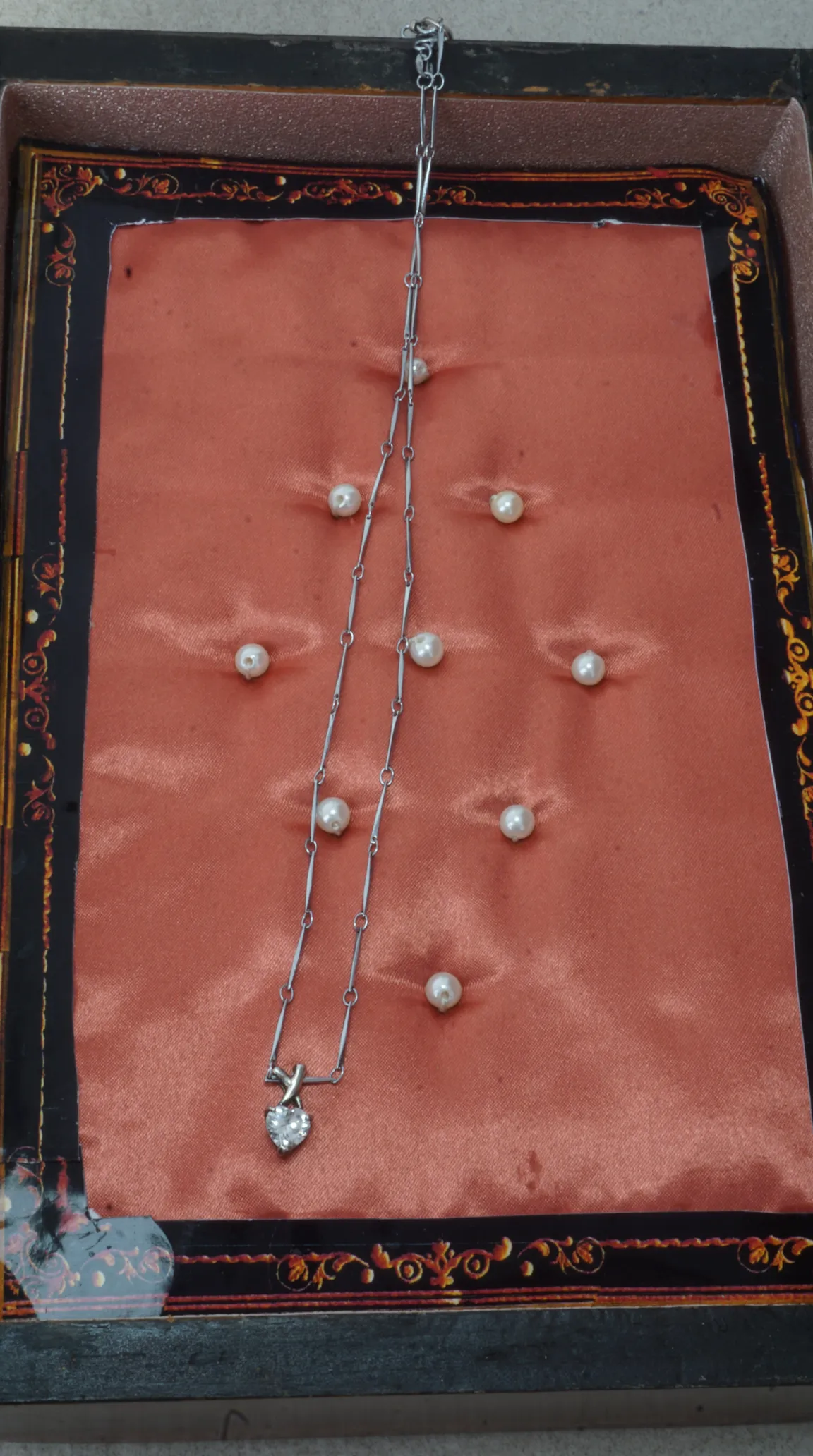Vintage silver-tone heart pendant necklace with sparkling clear stones, displayed in an ornate salmon satin jewelry box.