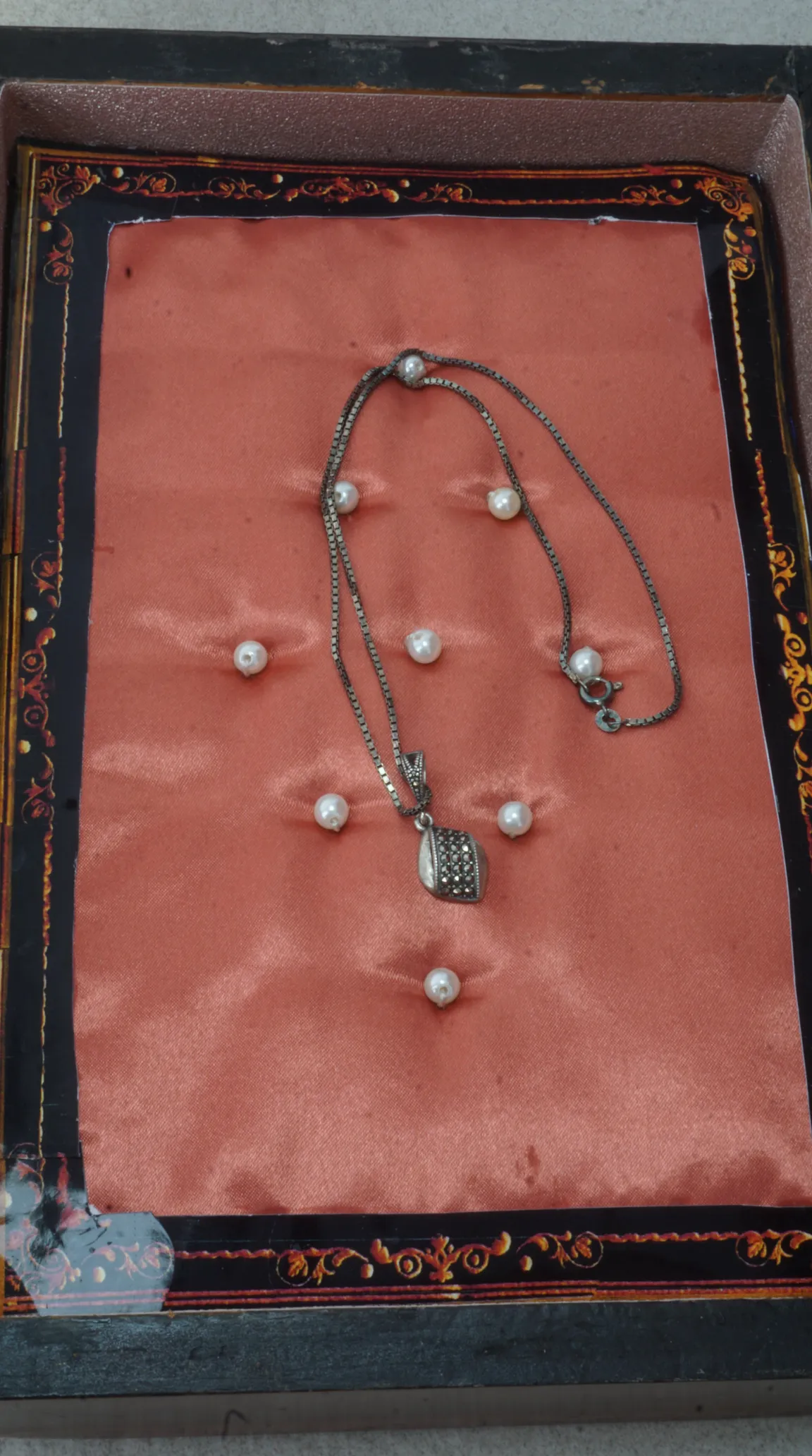 Vintage silver marcasite pendant necklace on peach satin lining inside ornate black and gold jewelry box.