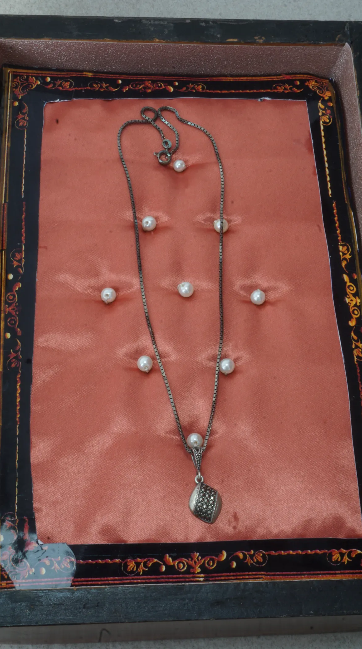 Vintage silver box chain necklace with marcasite and pearl pendant, displayed on pink satin in an ornate jewelry box.