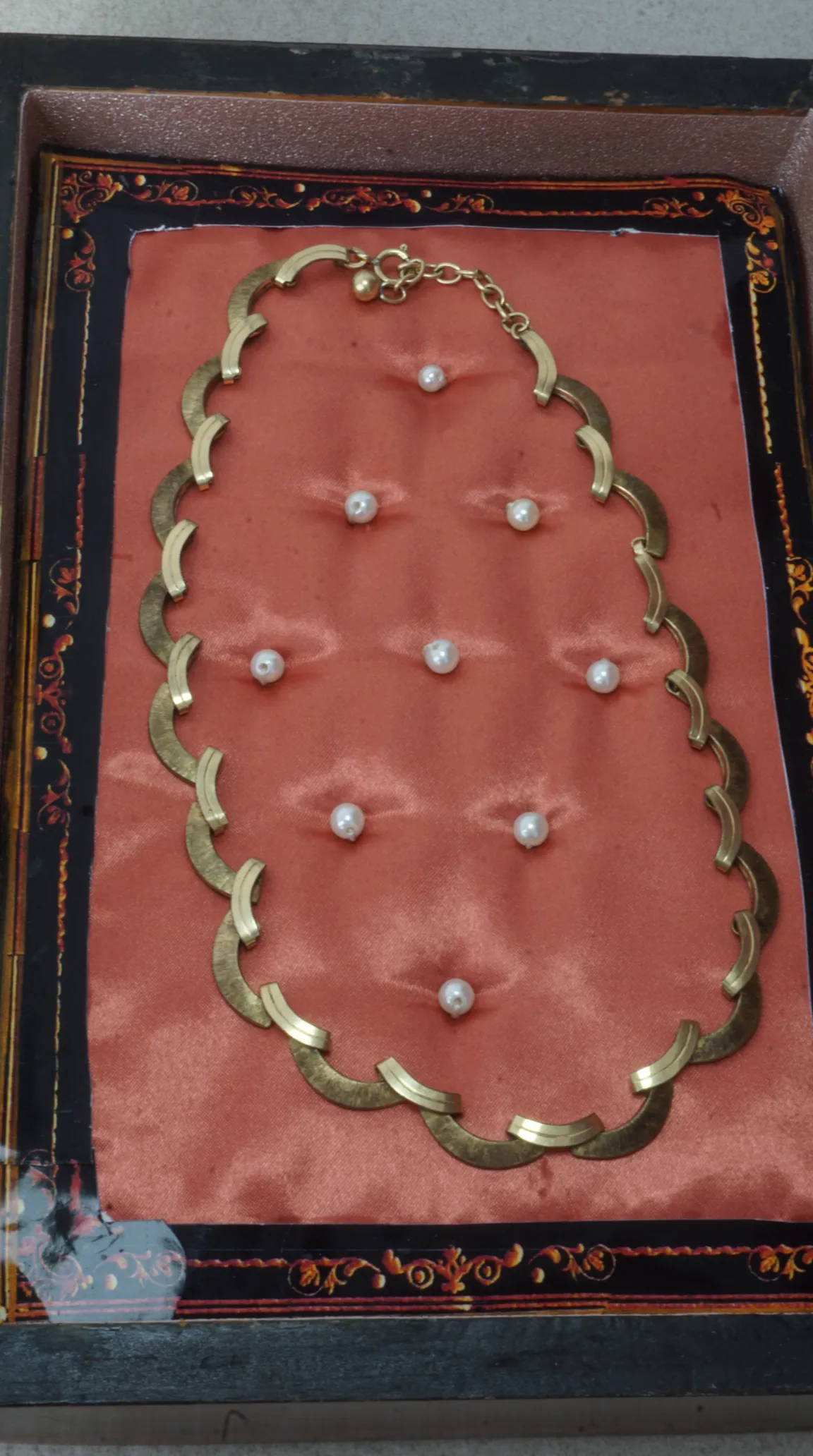 Vintage gold-tone geometric crescent link necklace displayed on coral fabric with scattered pearls in an ornate jewelry box.