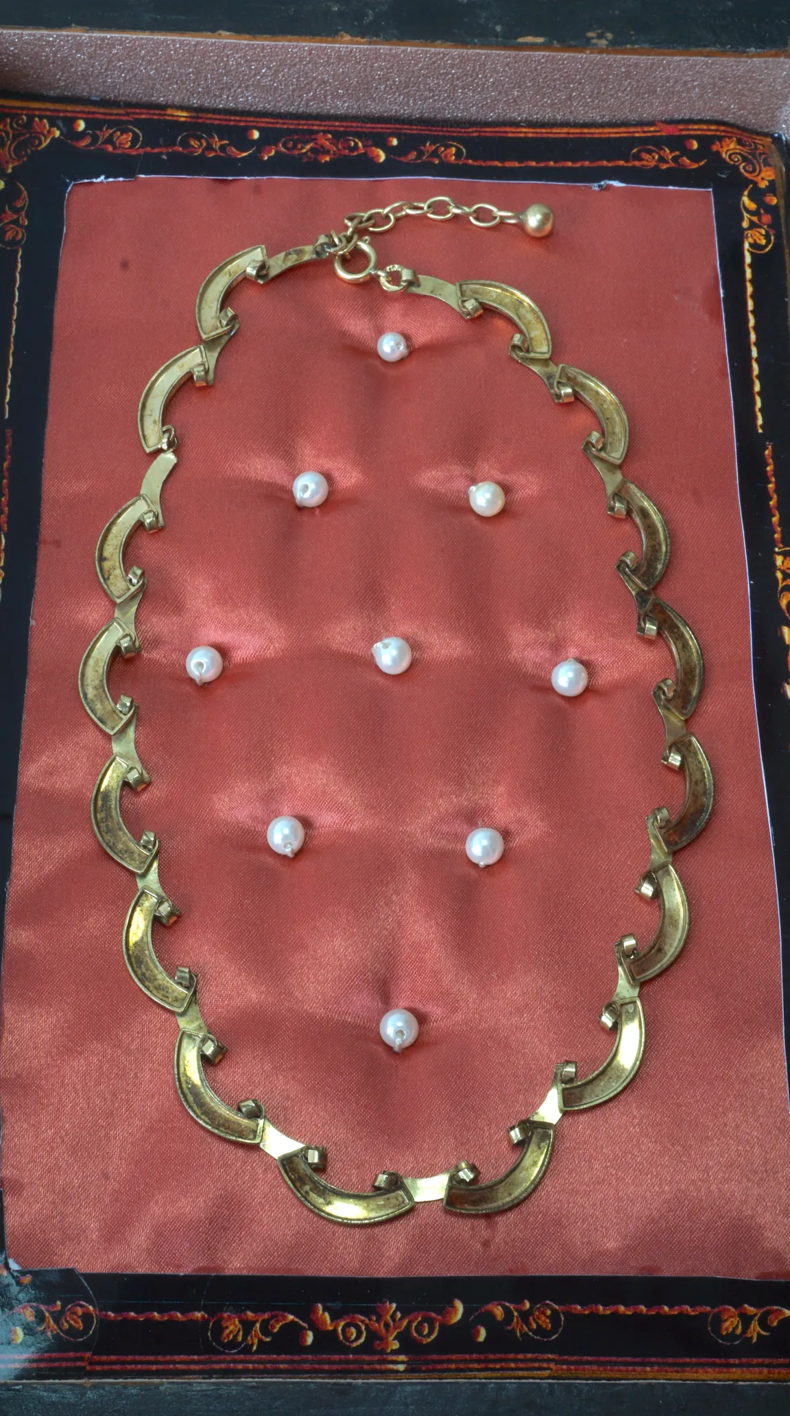 Vintage gold-tone crescent link necklace, with scattered pearls, displayed on a rose pink cushion in an ornate black box.