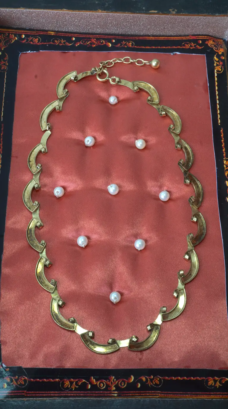 Vintage gold-tone crescent link necklace, with scattered pearls, displayed on a rose pink cushion in an ornate black box.