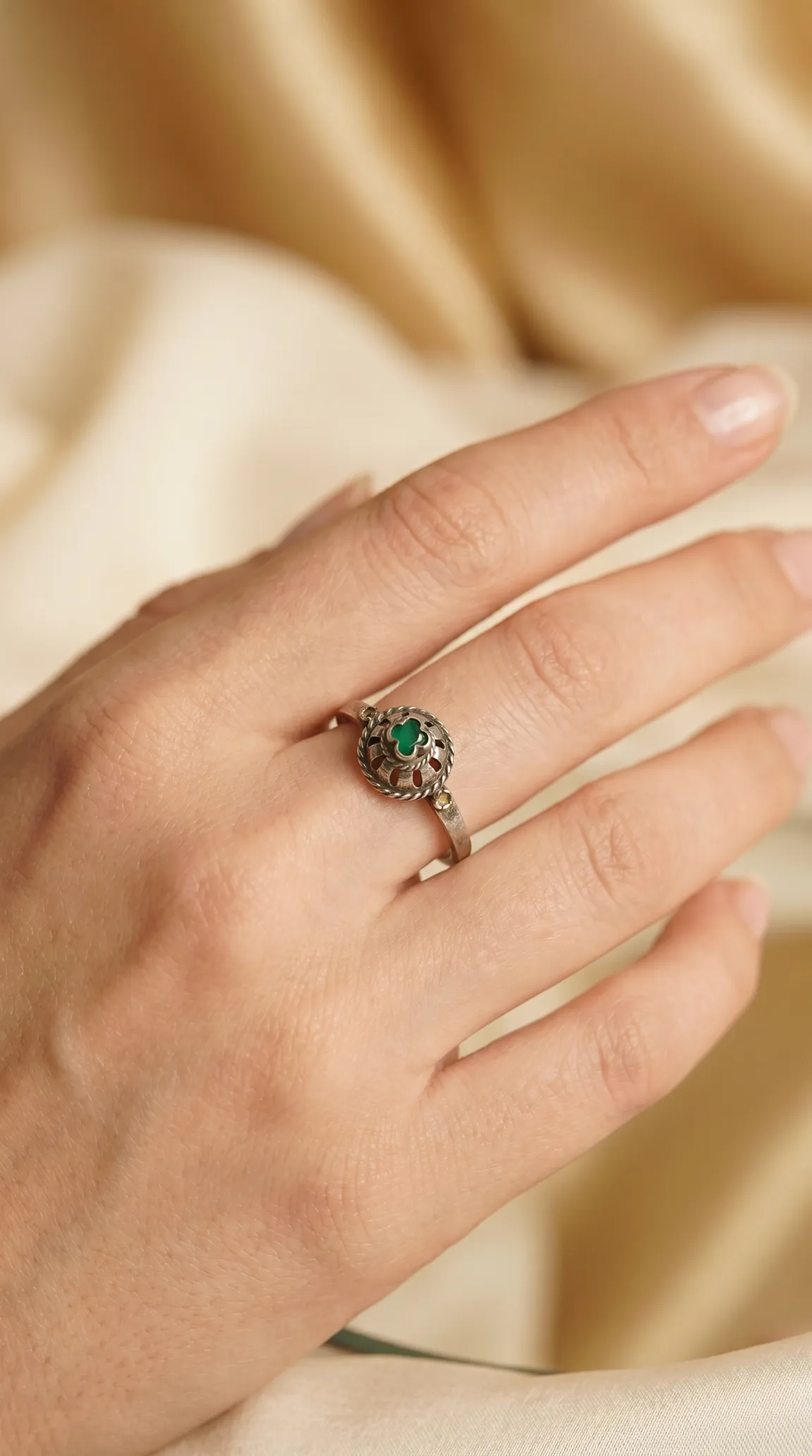 Vintage sterling silver ring with round green gemstone and clover-shaped filigree design, worn on a hand.
