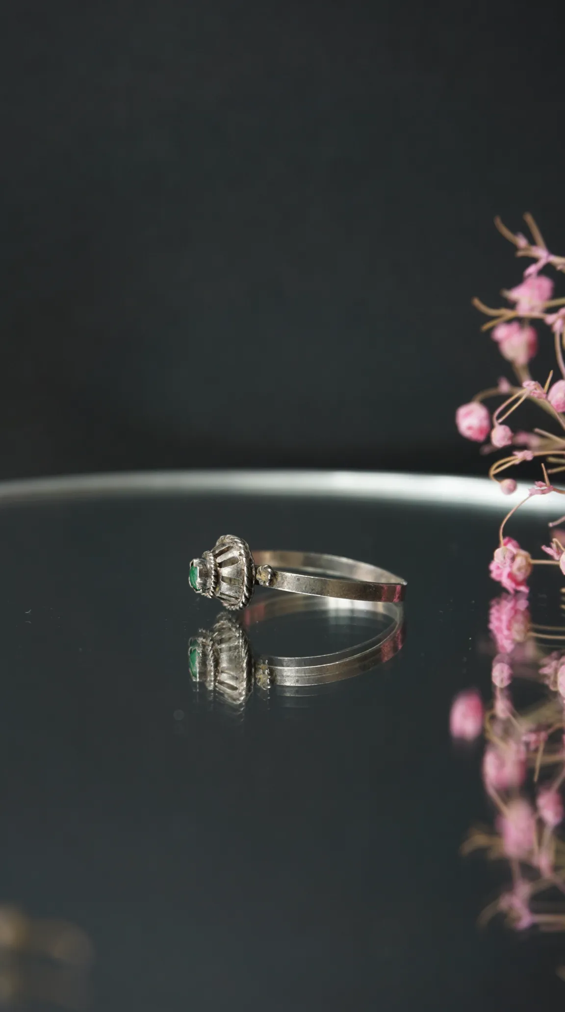 Vintage silver bracelet with emerald gemstone with intricate setting, reflected on a dark surface.