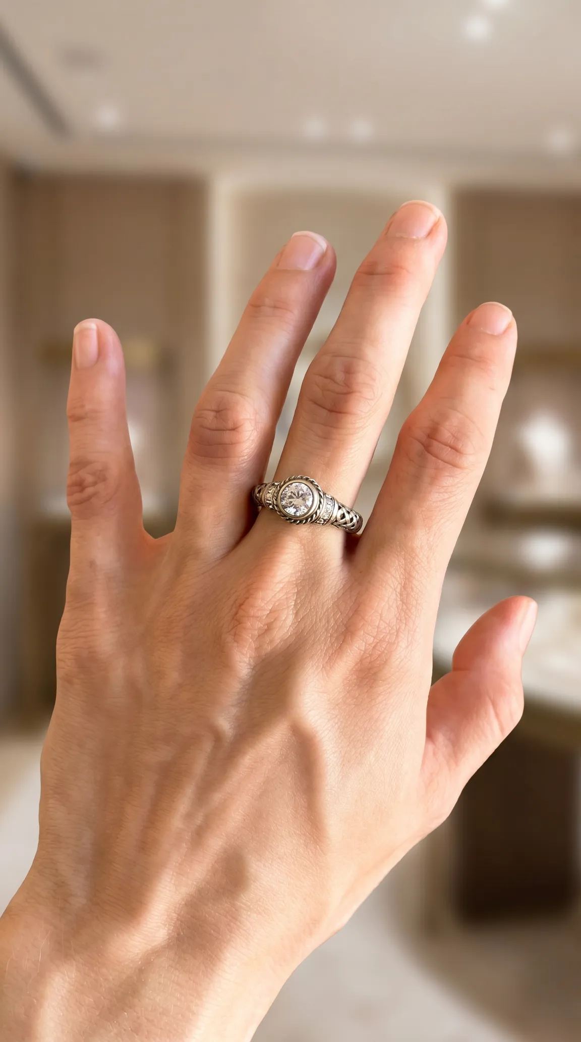 Vintage silver-tone ring on hand, round clear gemstone, intricate detailed band with rope edges and accent stones.
