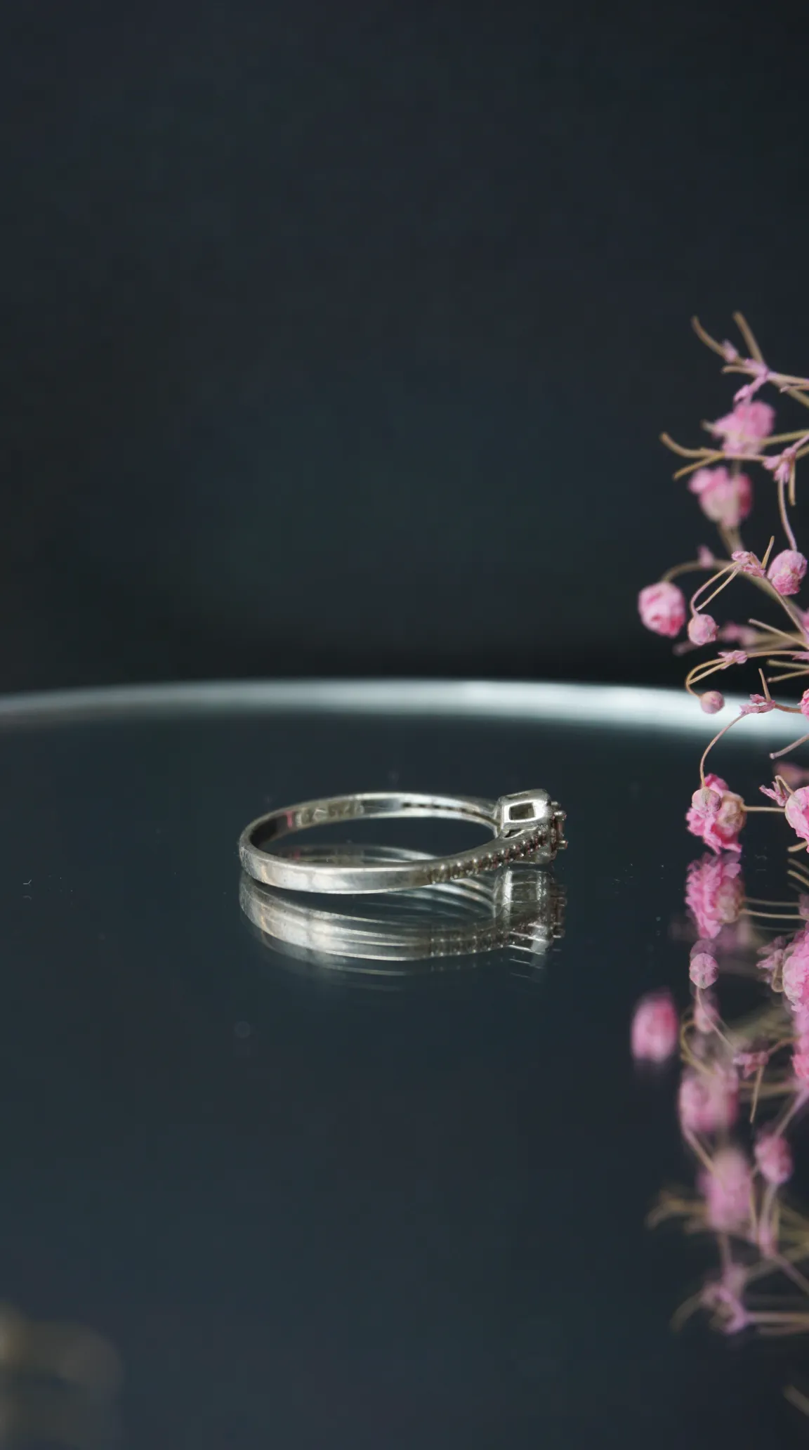 Vintage sterling silver ring with subtle gemstone accents on reflective dark surface with pink dried flowers.