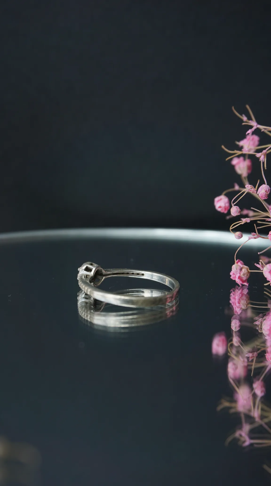 Vintage silver diamond ring on reflective surface with pink flowers.