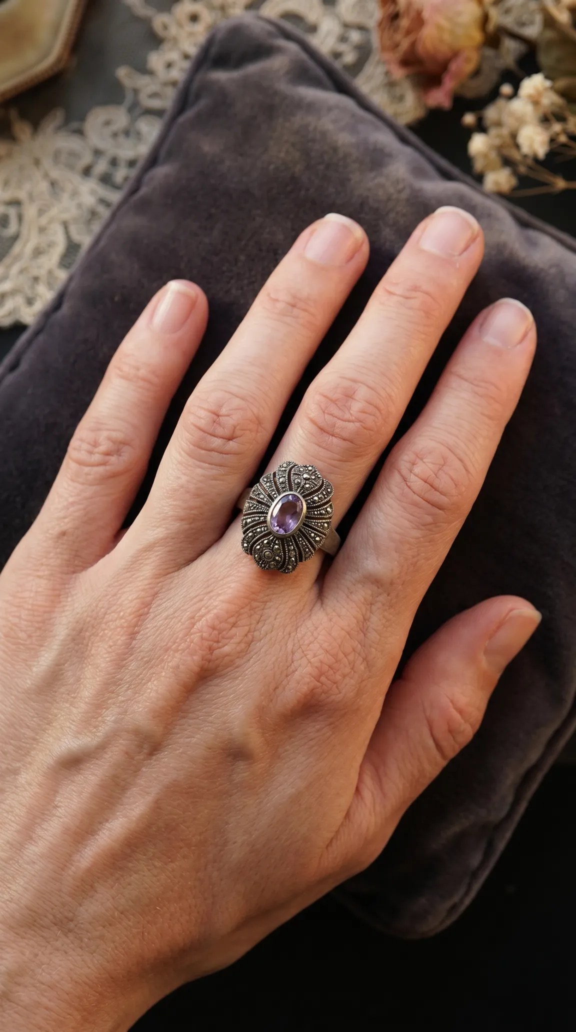 Vintage sterling silver marcasite ring with oval purple amethyst gemstone, worn on a hand.