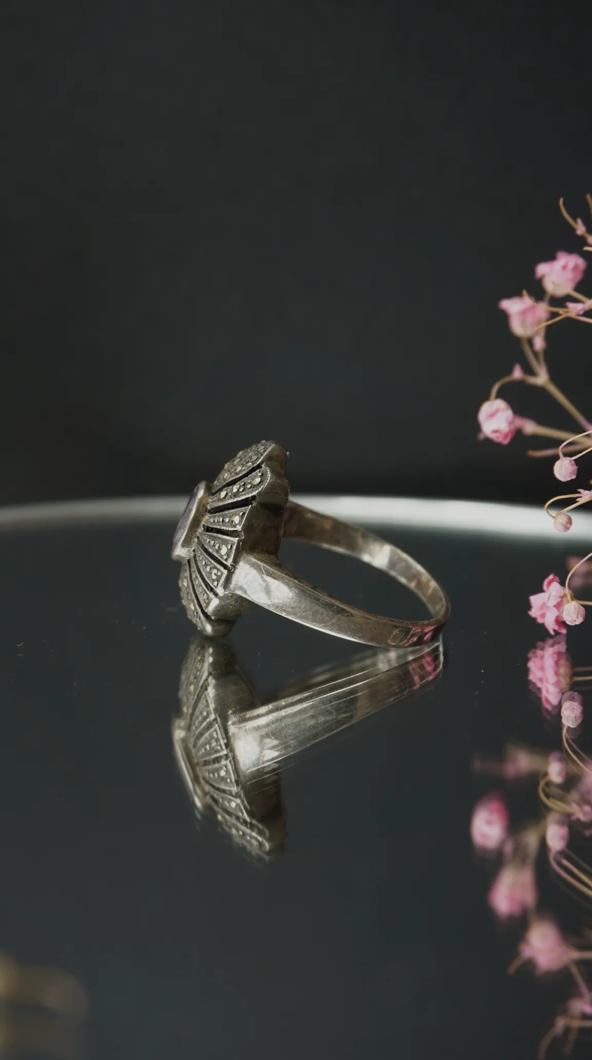 Vintage sterling silver Art Deco style ring with marcasite and purple amethyst gemstone, displayed on a reflective surface.