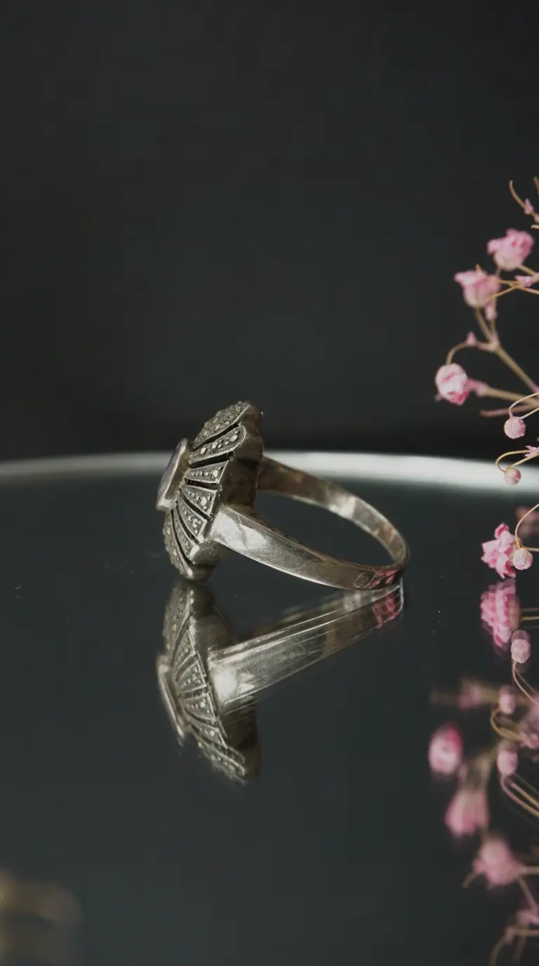 Vintage sterling silver Art Deco style ring with marcasite and purple amethyst gemstone, displayed on a reflective surface.