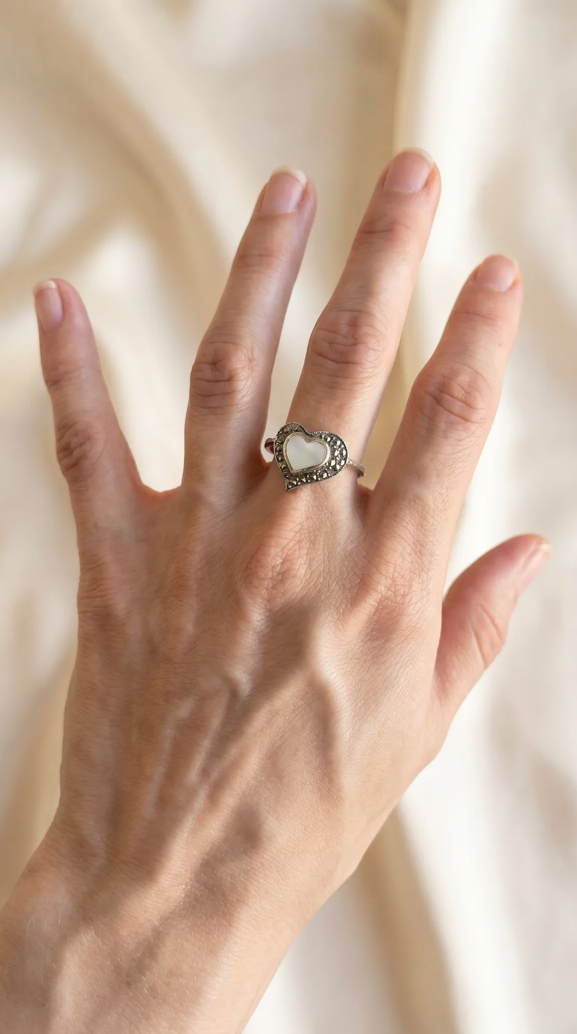 Vintage sterling silver heart ring with mother of pearl inlay and marcasite accents on a hand.