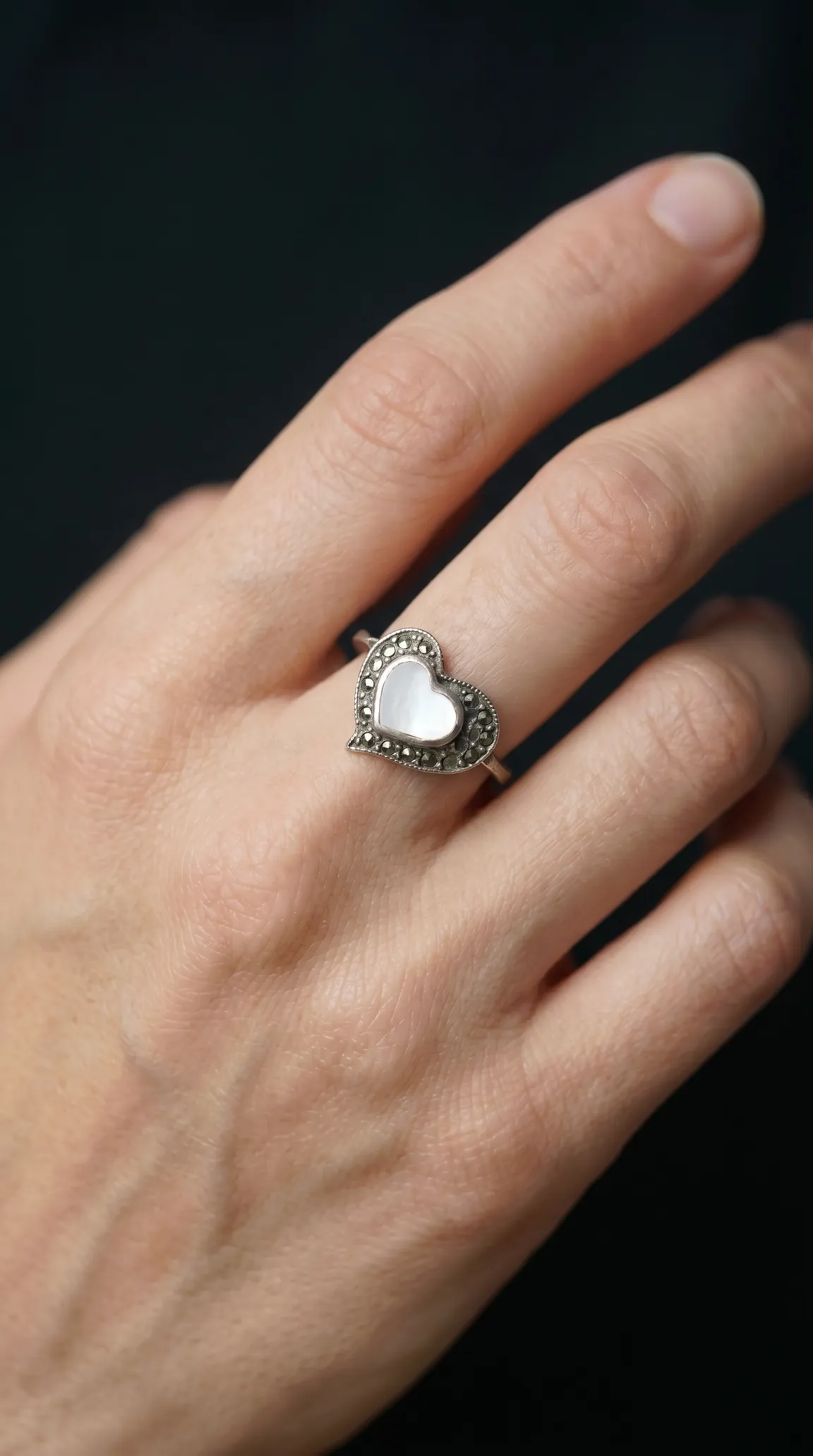 Vintage sterling silver heart ring with mother of pearl inlay and marcasite accents on a woman's hand.