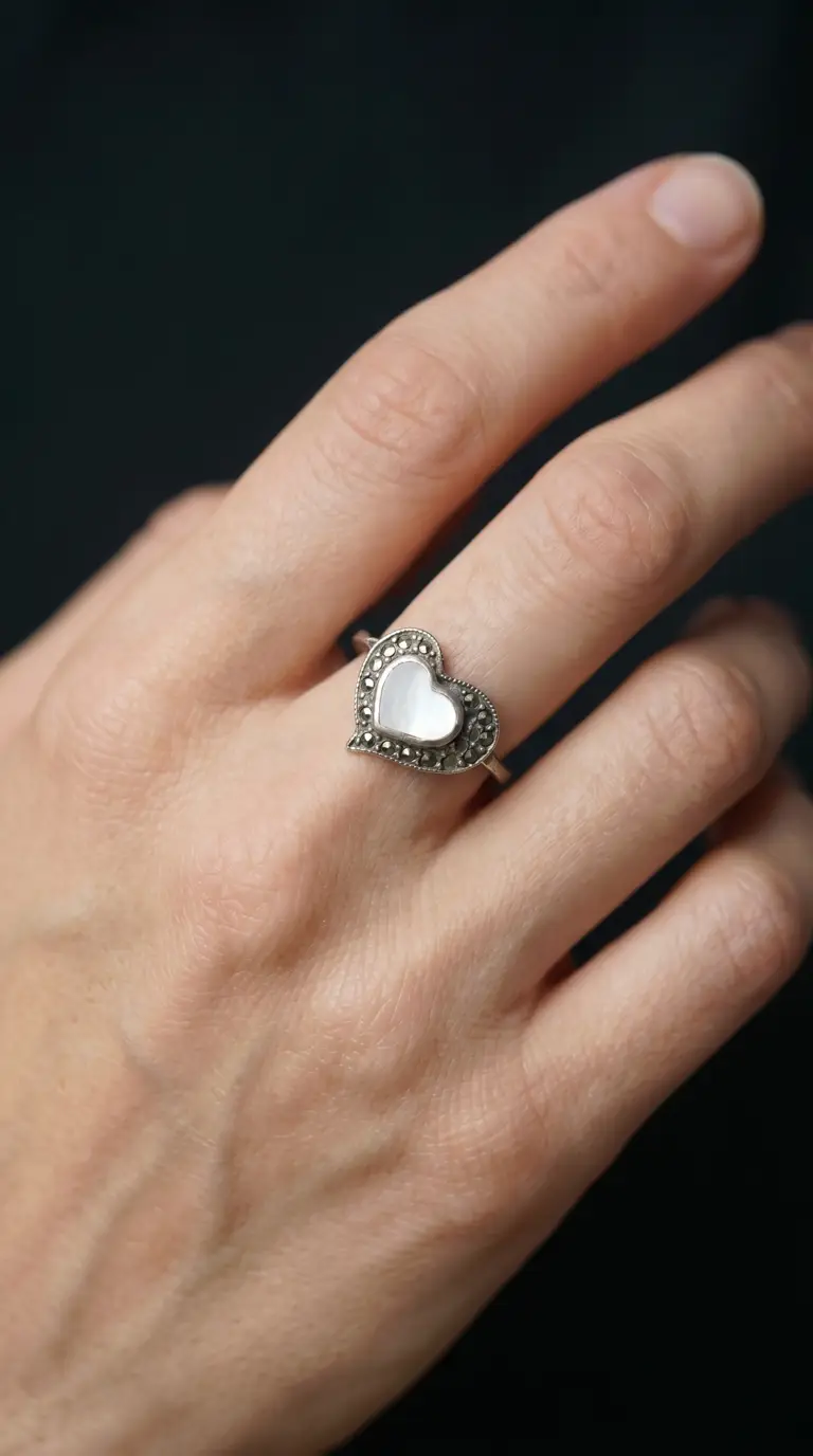 Vintage sterling silver heart ring with mother of pearl inlay and marcasite accents on a woman's hand.
